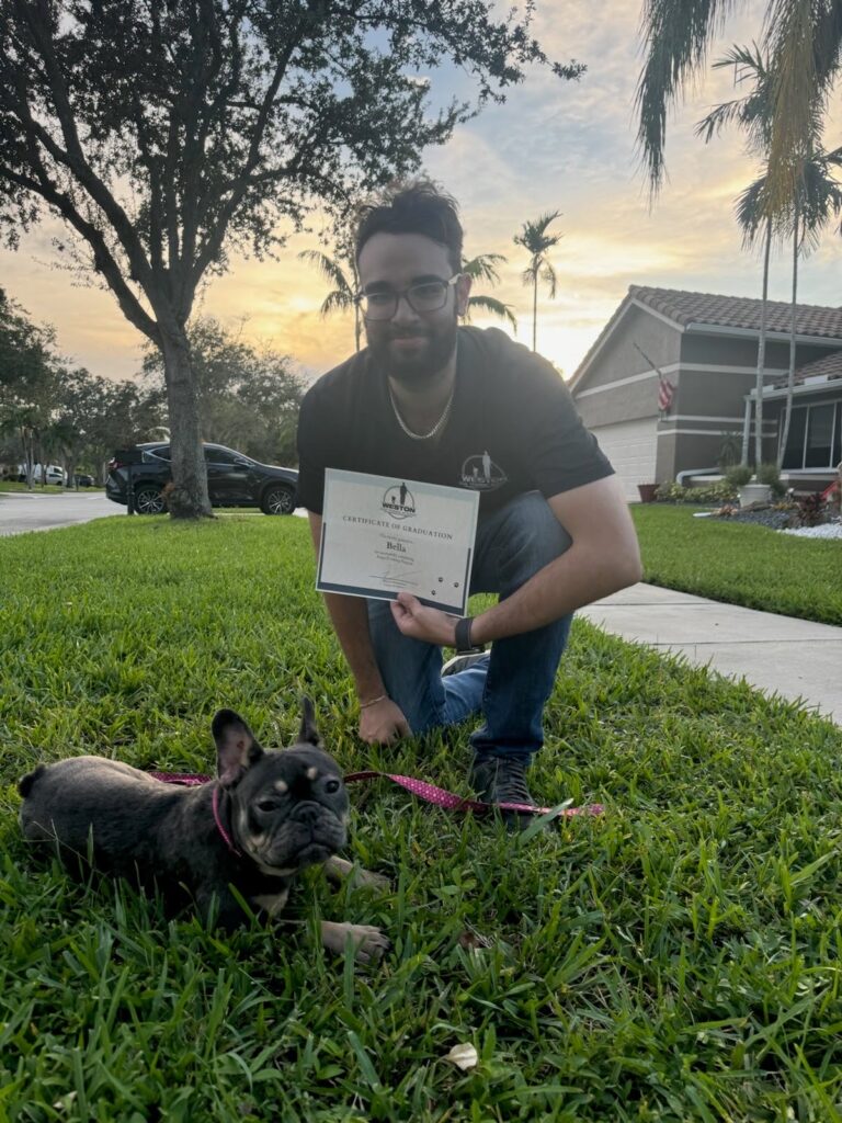 Trainer holding the diploma in front of dog laying on grass.